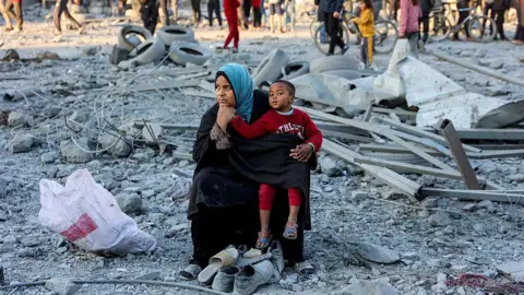 A woman child sit among grey rubble, pensively. 