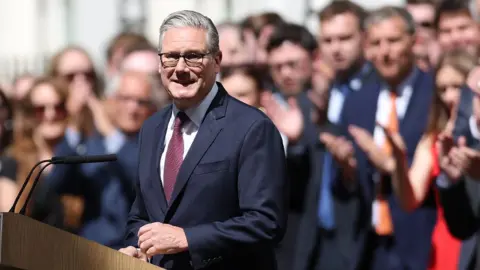 Keir Starmer smiling after giving final speech as Prime Minister on Downing street wiyth clapping crowd behind him