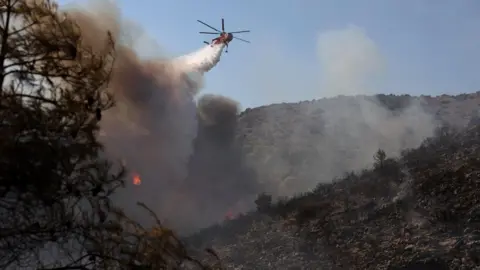 EPA/Shutterstock A firefighting helicopter operates to extinguish a wildfire on Salamina Island