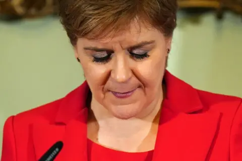 Getty Images Nicola Sturgeon announcing her resignation arsenic  archetypal  minister. She is looking down   from the camera and is wearing a reddish  overgarment   with a reddish  top