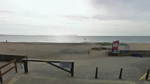 Google Gate and bollards at entrance to sandy beach with beach warning sign by low wall