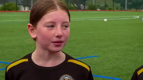 BBC Lily on a football pitch wearing Newport county girls academy strip