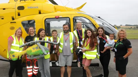 HIOWAA The family all wearing hi-vis jackets and standing in front of a yellow helicopter.