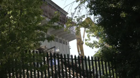 LDRS A demolition excavator works beside the former school building as debris is cleared from the site.