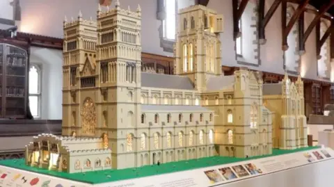 A model of Durham Cathedral crafted from pale yellow Lego bricks. It replicates the Romanesque building, with its tall central crossing tower and two western towers, and its rows of windows are illuminated from within. 