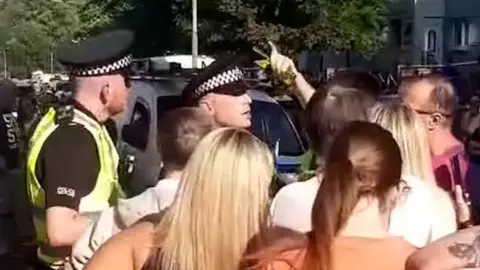Video grab of two police officers talking to a group of people who are pictured from behind