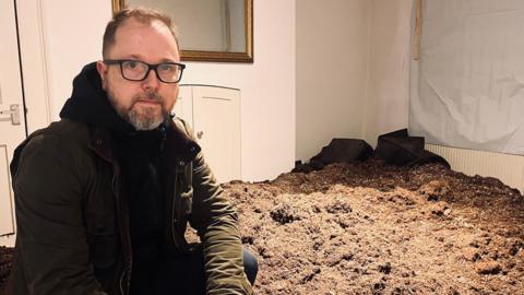 Charles Reeves stands in disbelief amidst the staggering ten tonnes of soil Charles Reeves stands in disbelief amidst the staggering ten tonnes of soil dumped by cannabis criminals in his bedroom.