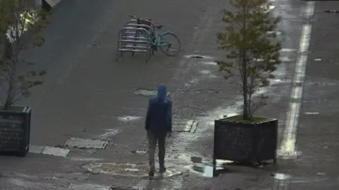 Man walks along wet Edinburgh pedestrian walkway wearing hoodie