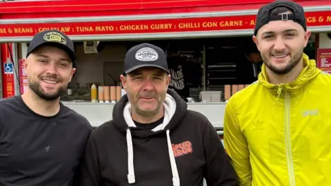 Spud Bros Jacob, Tony and Harley Nelson standing by the van. All are wearing black baseball caps and smiling, Tony has stubble and the boys have short dark beards.