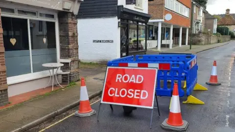 A Road Closed sign with a fenced off area in a village street