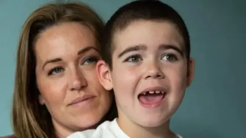 CLC PORTRAITS A woman on the left with brown hair behind a boy with his mouth open. A light blue background is behind them.