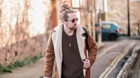 Chris Illingworth A professional picture of Mitchell Lucas. He is photographed looking away from the camera wearing sunglasses, while walking down a narrow street. 