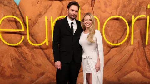 Reuters Euphoria creator Sam Levinson and actress Sydney Sweeney (right) attending the LA premiere for the new series earlier this week. He is wearing a black suit and tie and she is wearing a white dress.