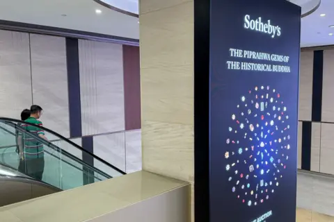 The image shows an billboard advertising the sale of the Buddha jewels, which are shown arranged in a circle. They come in a range of colours, and some are shaped like flowers. 