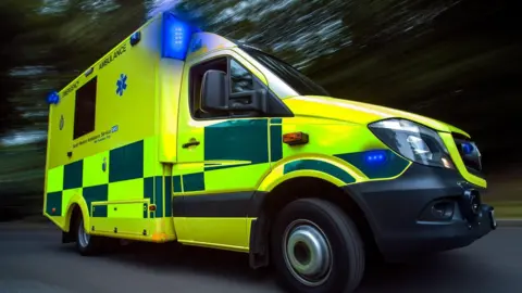 Ambulance travelling from left to right it has its lights flashing.