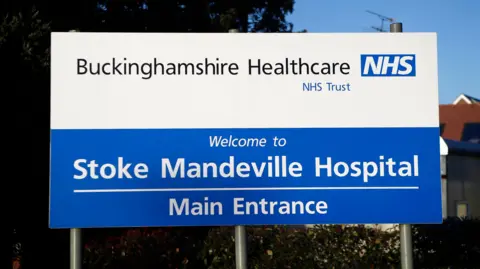 A white and blue sign at the entrance to Stoke Mandeville Hospital, advertising the hospital.