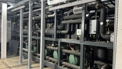 George Carden/BBC Inside the energy hub where there's air source heat pumps, piping, tanks and gauges.