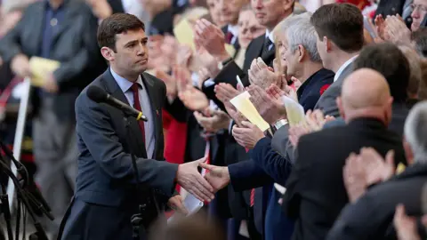 Getty Images Andy Burnham shakes hands with a member of the crowd, applauding after his speech at Anfield Stadium in 2014.