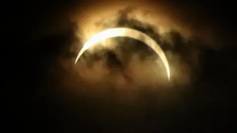 BBC Weather Watchers/MackemIan The solar eclipse captured in Sunderland. A small section of yellow sun is visible through thin clouds. The sky around it appears dark.