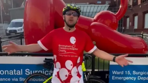 Andy Gulch A man standing in a red top in front of Birmingham Children's Hospital