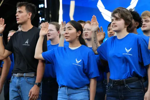 BULL STOCK MEDIA A ling of young people in blue and black Space Force logo t-shirts hold up their right hand as they take an oath