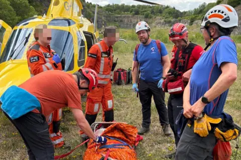 Edale MRT A casualty strapped in to a stretcher near to a helicopter, surrounded by rescuers and medics