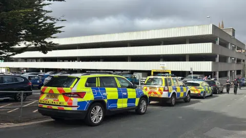Three police cars parked outside a concrete multi-storey car park