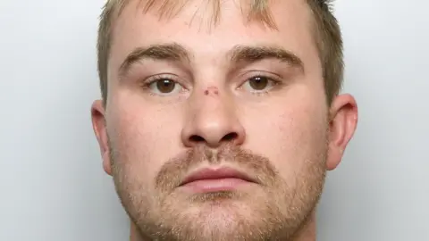 A custody image of a young man with light hair and facial stubble.