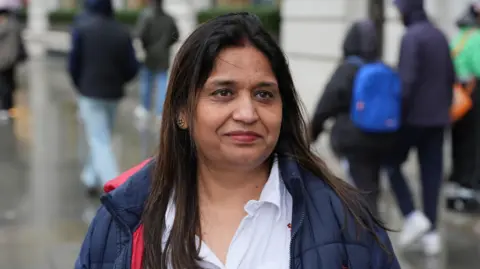 PA Seema Misra smiling with people walking in the street behind her