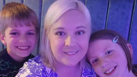 A boy, a woman with blonde hair and girl smiling