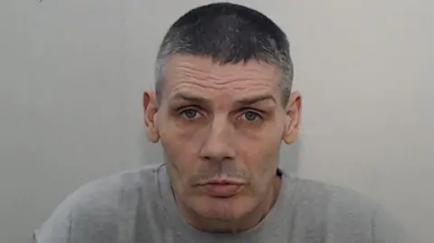 GMP Police mugshot of Peter Pitt. He has very short grey hear and is wearing a light grey t-shirt.