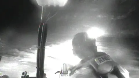 A blurry black and white photo showing an RNLI crew member and bright lights.