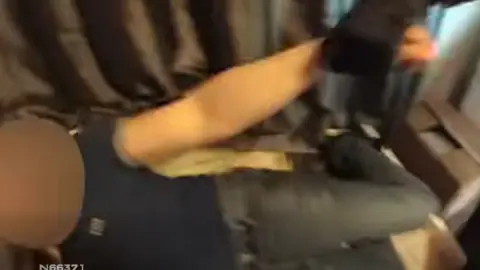 Nottinghamshire Police Police body-worn cameras showing the moment a man was found lying in a child's-size bed in an empty house. An officer's arm can be seen grabbing the man's up and pulling him up as he is woken up.