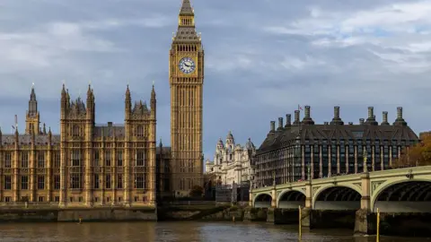 The Elizabeth Tower, known as Big Ben, and the Palace of Westminster beside the River Thames, with Westminster Bridge in the foreground under cloudy skies.