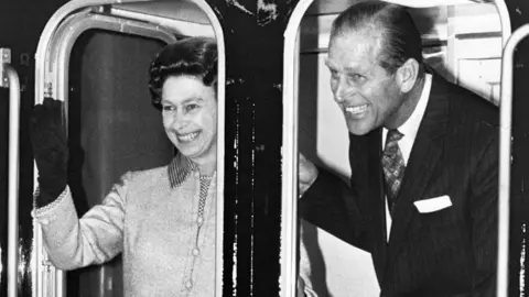 Queen Elizabeth II and her husband Prince Philip, Duke of Edinburgh, smile and wave as the Royal train pulls out of Euston n 1977