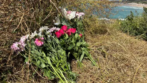 Red, pink and white flowers left on the dunes above the scene of the deaths at south Fistral