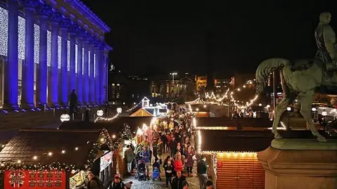 Liverpool Christmas Market at night showing traditional wooden chalets lit up on St George's Plateau with St George's Hall lit up with white lights.