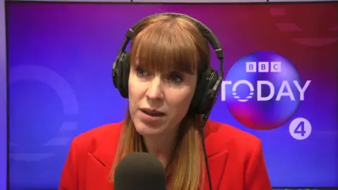 Angela Rayner in front of a mic wearing headphones and a red blazer.