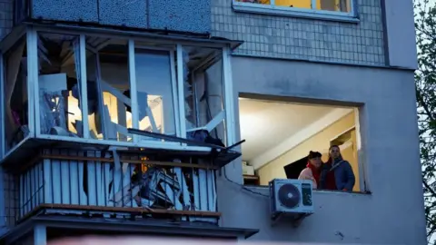 Reuters Two women look out of a window of an apartment block at the site of a Russian missile strike in Kyiv