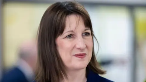 Getty Images Chancellor Rachel Reeves with shoulder length brown hair and a navy blue jacket smiling