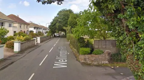 Google Street View image of Wellington Road in St Helier. Houses are on both sides of the roads. Several trees in full bloom are also dotted along the road.