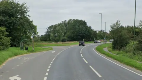 A Google Street image of a bus stop to the left of a road.