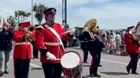 Three men in red uniforms play the drums