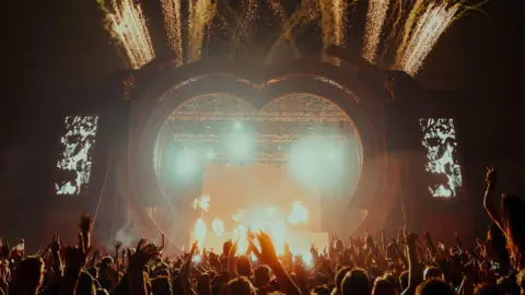 @Eljaybriss A stage with a large heart around it, and a crowd with their hands in the air in the foreground