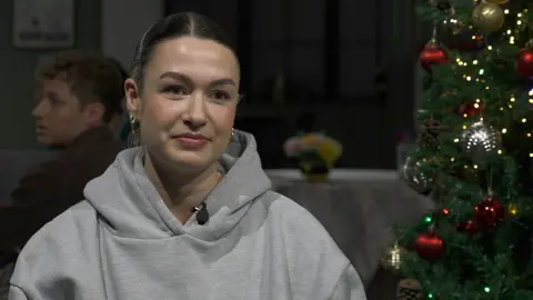 Freya Volk in a grey hoodie sat next to a Christmas tree