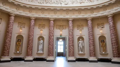 Stowe House A circular hall with tall pink‑marbled columns, ornate wall carvings and statues displayed in recessed alcoves. 