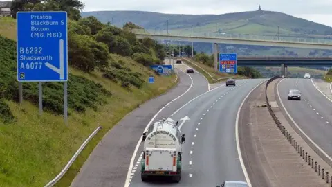 Vehicles on either side of the M65 at a slip road junction, with Darwen Hill and the Jubilee Tower on the summit in the background