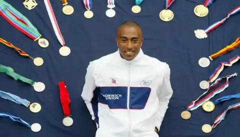 Getty Images Man in white sport jacket lies on the ground surrounded by medals
