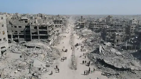 Getty Images In an aerial view, people walk amid the destruction in Gaza City in the northern Gaza Strip. Every building visible is a shattered ruin, stretching back to the distant horizon.