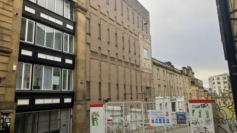 Tall sand-coloured brick buildings surrounded by fencing that protects pedestrians from construction work.